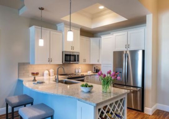 Wide shot of a spacious kitchen with stainless steel appliances and hanging ceiling lights.