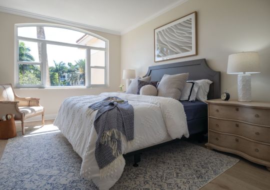 Cozy and spacious main bedroom with a large bed and open window inside of an Erickson Senior Living community apartment.
