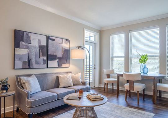Cozy living room with gray sofa, round coffee table, large windows, and dining area with natural light.