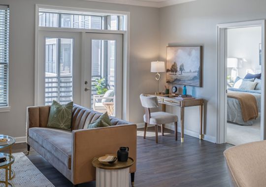 Bright living room with modern sofa, glass coffee table, large windows, and balcony access with natural light.