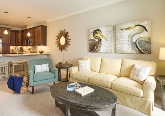 Spacious open-concept living room with cream sofa, accent chairs, and modern kitchen with granite countertops and stainless-steel appliances.