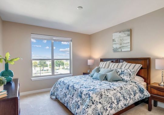 Bright bedroom with floral bedding, large window, wood furniture, and soft neutral decor.
