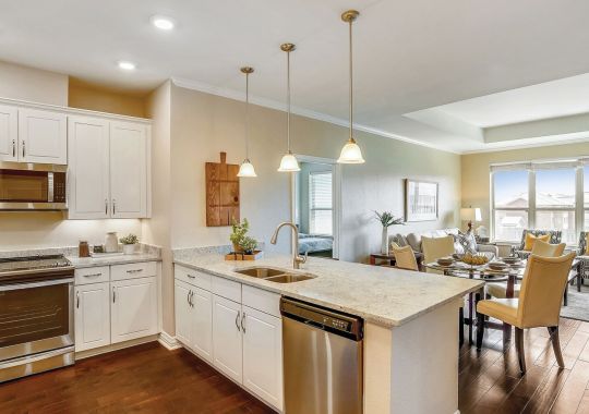 Spacious open kitchen and living area with white cabinetry, large island, wood flooring, and natural light.