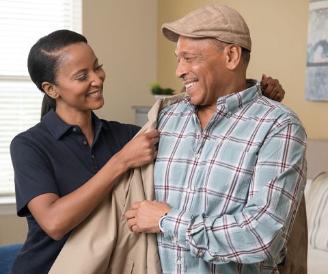 A cheery Erickson employee assists a smiling resident with putting on his coat.