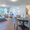 Wide shot of a bright and open living room, kitchen, and dining room in a two-bedroom apartment.