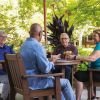 A multicultural group of four Erickson residents gather at a patio table laughing and talking. 