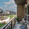 Spacious balcony at a senior living community apartment overlooking a beautifully landscaped courtyard with lush greenery, walking paths, and seating areas.