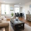 Bright and modern living room with neutral tones, featuring a beige sofa, wooden coffee table, accent chairs, and a large window.