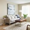 Bright and modern living room with neutral tones, featuring a beige sofa, wooden coffee table, accent chairs, and a large window with sheer curtains.