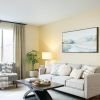A bright and airy living room with a sofa adorned with decorative pillows, coffee table, and a large window with an outdoor view.