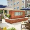 Outdoor courtyard with patio seating, blue umbrellas, garden landscaping, and a central brick fireplace feature.