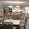 Spacious communal kitchen and dining area with a large island set with pastries, fruit, and coffee service, surrounded by light-colored cabinetry, stainless steel appliances, and multiple seating tables.