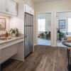 Compact kitchenette with granite countertops, white cabinets, and a small dining table, leading to two adjoining rooms with seating and decor.