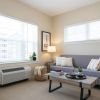Bright living room with large windows, a sofa, armchair, coffee table, side tables with lamps, and decorative plants and books.