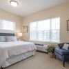 Bright bedroom with neatly made bed, armchair, dresser, and large windows.