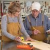 Older couple in a workshop measuring wood together with tools and aprons.