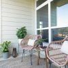 Cozy outdoor balcony with two wicker chairs, a small table, and potted plants, creating a relaxing seating area with natural light.