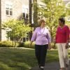 Two older women walking together on a sunny path in a landscaped residential community, smiling and chatting.