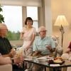 Group of older adults gathered in a bright living room, sitting together and enjoying drinks and conversation around a coffee table.