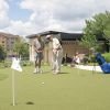 Two older men playing golf on a putting green in a landscaped outdoor area. 