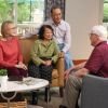 Group of older adults sitting together in a cozy living room, engaged in friendly conversation around a coffee table.