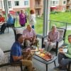 Group of older adults relaxing and socializing on a covered patio, enjoying drinks and appetizers together with a landscaped courtyard in the background.
