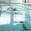 Older adult swimming laps in an indoor pool with lane dividers in a senior living fitness facility.