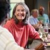 Smiling older adults enjoying drinks and conversation at a bar, with wine glasses and small plates of food in a warm, social setting.