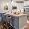 Bright modern kitchen with white cabinets, granite island with bar stools, stainless steel appliances, and open layout.