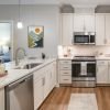 Contemporary kitchen with white cabinetry, stainless steel appliances, granite countertops, and warm wood flooring.