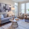 Cozy living room with gray sofa, round coffee table, large windows, and dining area with natural light.