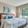 Bright bedroom with large windows, plush bedding, wood furniture, and peaceful outdoor views.