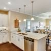Spacious open kitchen and living area with white cabinetry, large island, wood flooring, and natural light. 