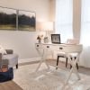 Modern home office with white desk, accent chair, natural light, and contemporary decor.